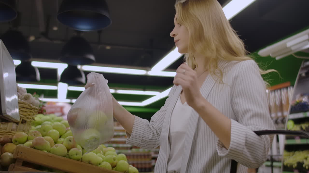 Young Woman Weighing Apples on the Electronic Scales. Housewife Shopping in a Supermarket in the Department of Fruit and Vegetables. Slow Motion. Sale Shopping Consumerism and People Concept