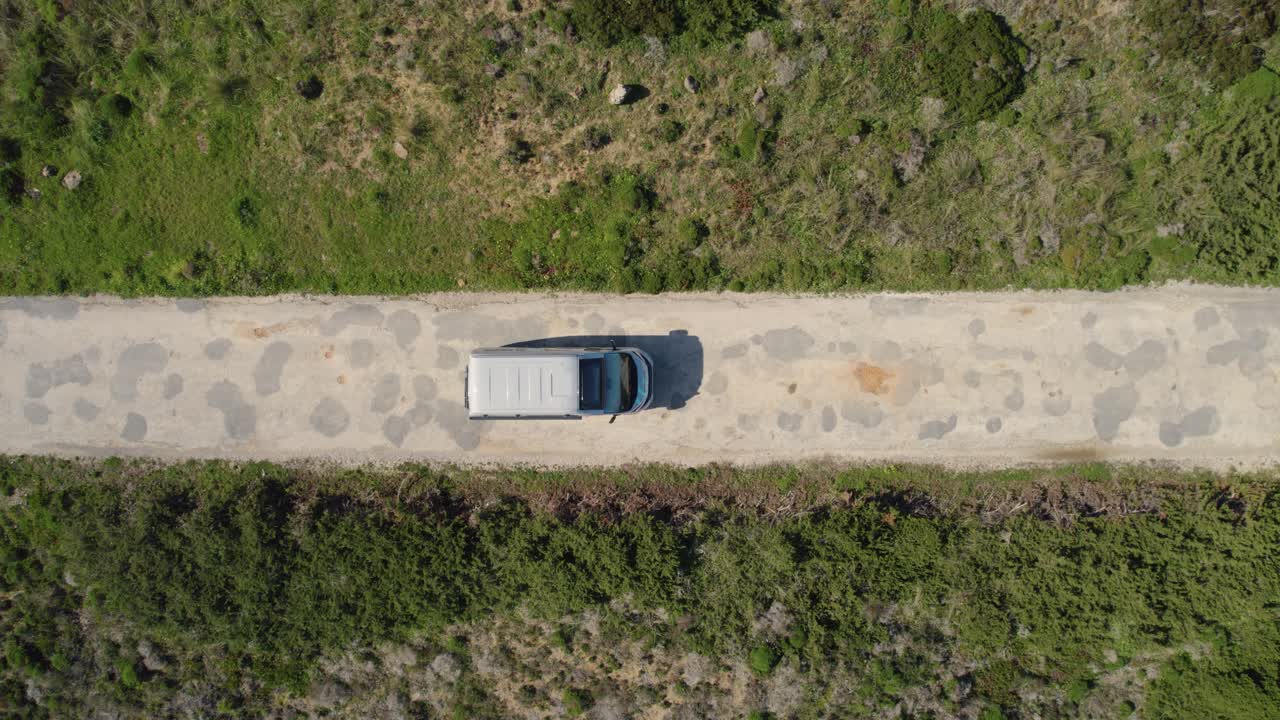 Veduta drone dall'alto che segue un camper a noleggio lungo una piccola strada rocciosa