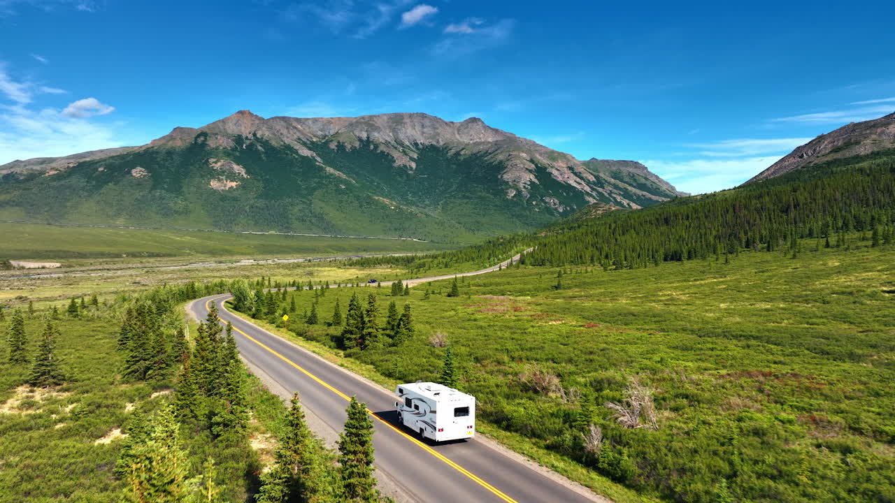 Following a campervan travelling by the road in the valley on sunny day. Spectacular mountains at backdrop