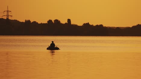 boat with a fisherman in the sunset light floats slowly on the lake. silhouette of a man sitting in a boat and fishing on the orange background of beautiful sunset in the river.