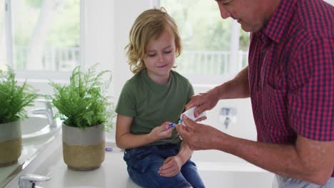 Caucasian-grandfather-helping-his-grandson-to-apply-toothpaste-on-toothbrush-at-home