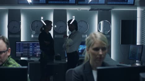 government cybersecurity agency senior officers have discussion while team of professionals work on computers in cooperation with military. specialists working on computers in system control room.
