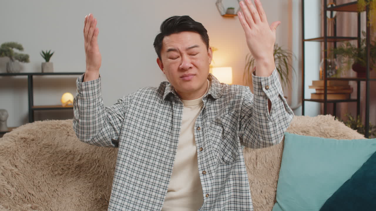 Upset young man making disrespect gesture disappointed in fail results bad news on sofa at home