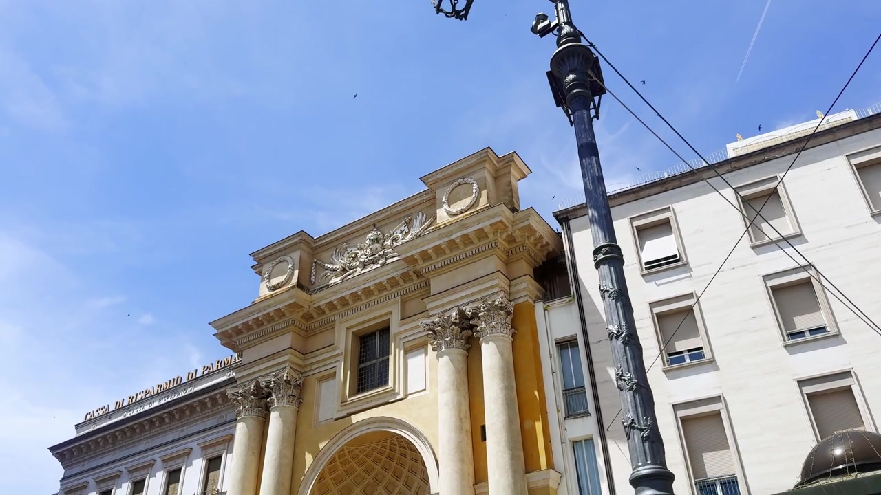 Vista dall'alto verso il basso da un lampione in ghisa ornato alla facciata neoclassica di San Pietro Apostolo in Piazza Garibaldi, Parma, sotto un cielo azzurro limpido