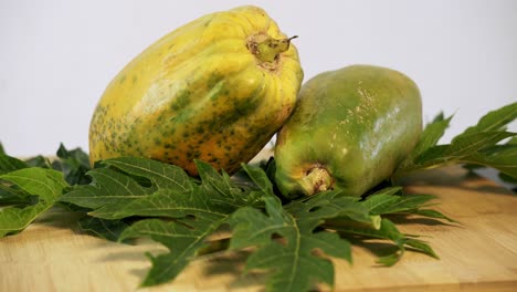 Langsames-Heranzoomen-Auf-Zwei-Reife-Papayas-Mit-Papayablättern-Drumherum-Paw-Paw-Vegan-Vegetarisch-Obst