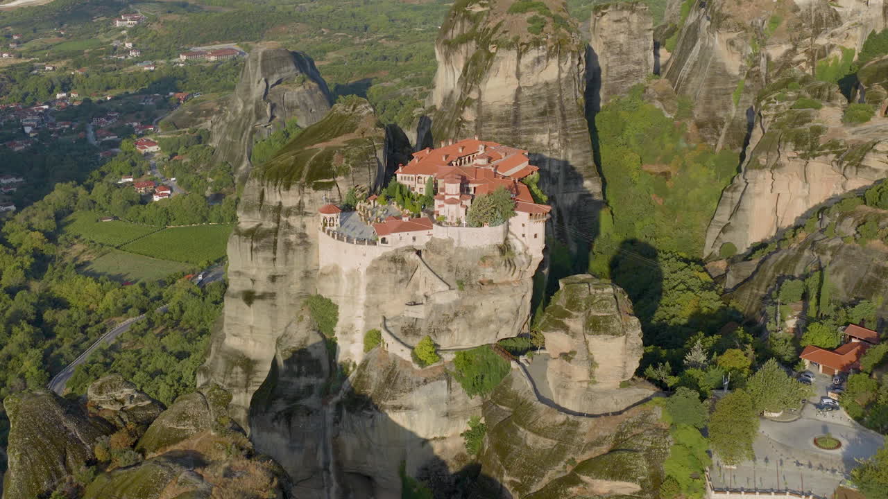 Cinematic aerial view of Meteora monastery in Greece perched on towering cliffs, dramatic rock formations and lush green valley create a breathtaking historic scene
