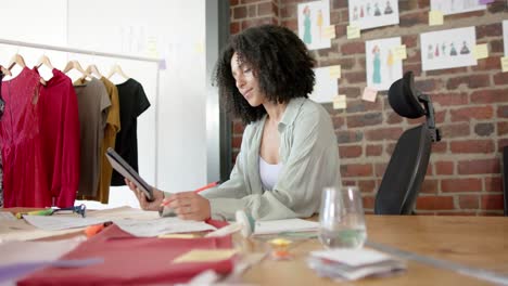 Portrait-of-happy-biracial-asian-female-designer-using-tablet-in-fashion-design-studio,-slow-motion