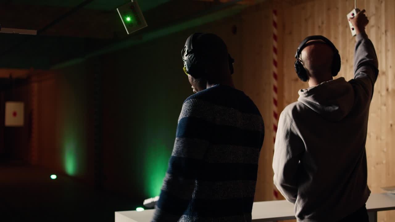 hombre recargando pistola en un campo de tiro interior junto a amigos disparando a objetivos