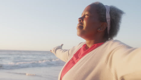 happy senior african american woman widening arms at beach, in slow motion