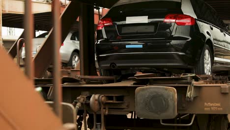 Cars-loaded-on-a-train-carriage,-partially-covered,-at-an-industrial-depot