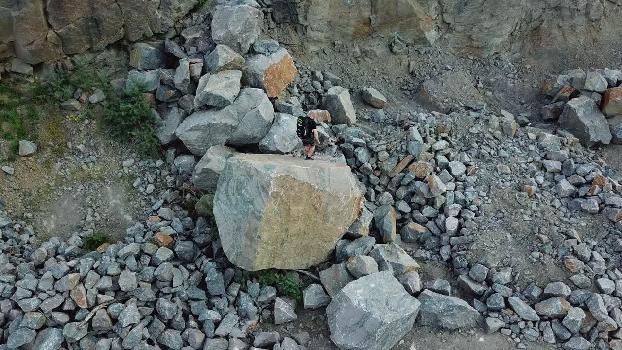 Top view of the young tourist going down from the big stone outdoors. Extreme hiker with rucksack walking on the rocks in summer day.