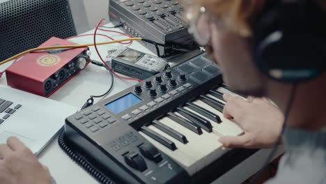 musician using synth and laptop at home recording studio