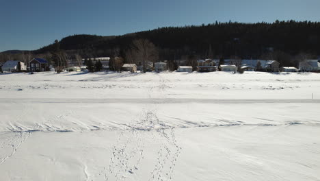Fliegende-Drohne-über-Spuren-Im-Schnee-Auf-Einem-Zugefrorenen-See-Im-Winter-In-Kanada