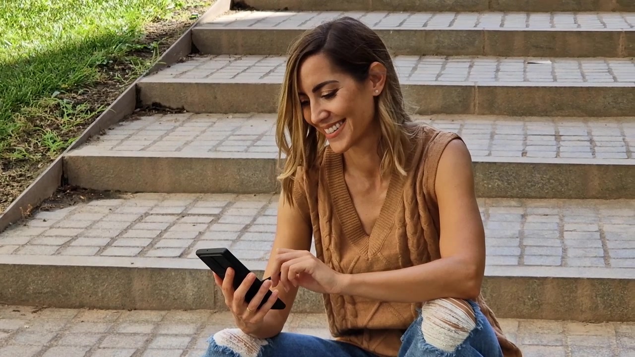 Mujer positiva usando su smartphone con un lápiz o stylus al aire libre.