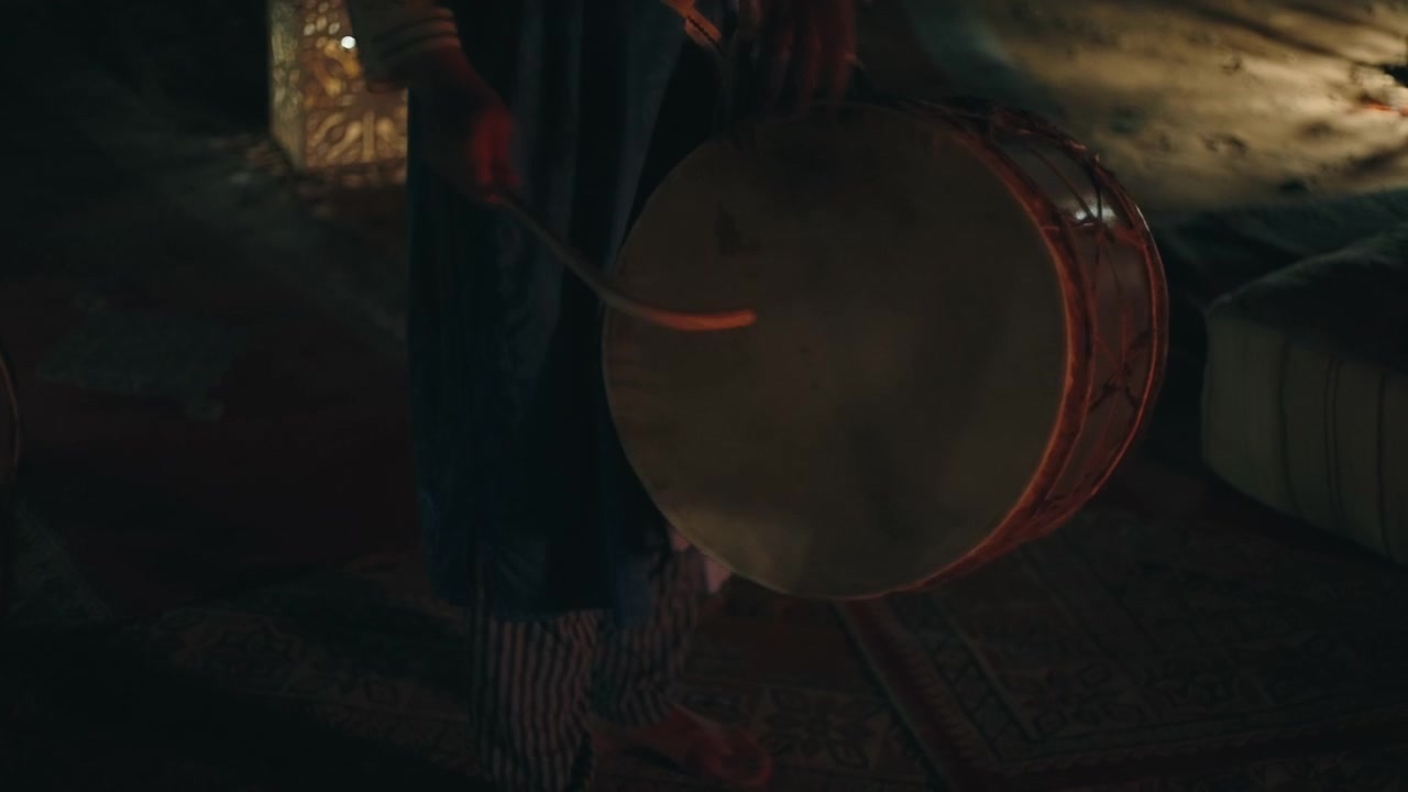 Traditional Berber bendir frame drum with animal skin membrane being played at a desert campfire night in Morocco