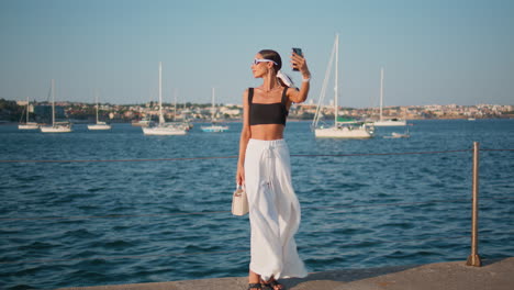 mujer elegante tomando una selfie en un muelle junto al mar