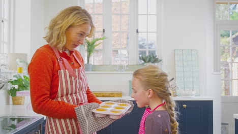 granddaughter smelling freshly baked cupcakes that grandmother has taken out of the oven in kitchen