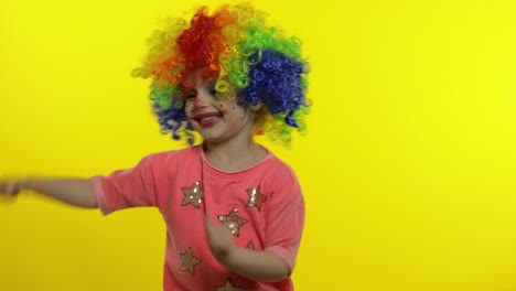 little child girl clown in colorful wig waving hands, having fun, smiling. halloween