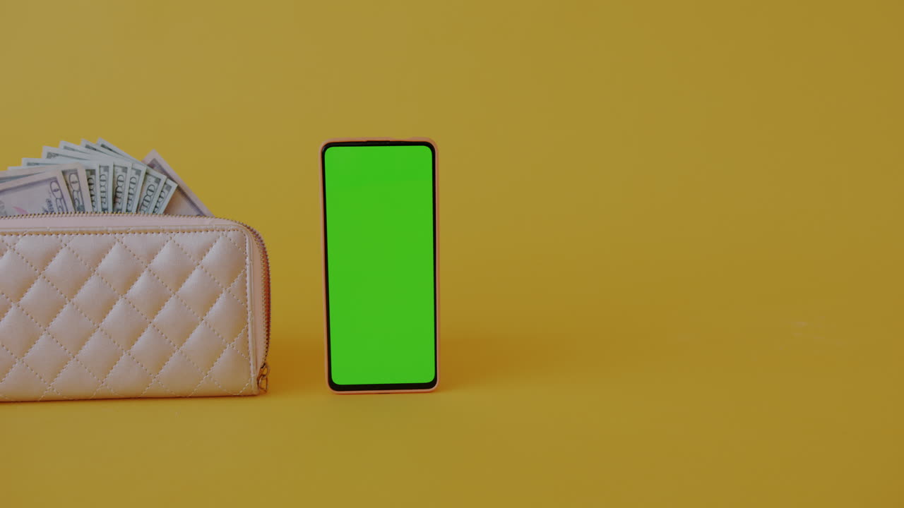 Wallet with money and a green screen phone on yellow background