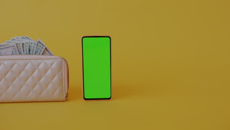 wallet with money and a green screen phone on yellow background