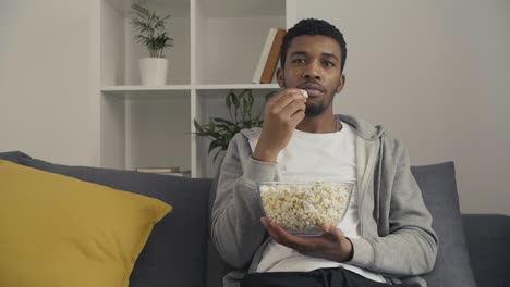 macho joven mirando atentamente una película y comiendo palomitas de maíz
