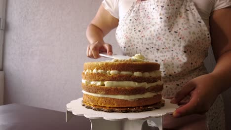 Lateinische-Frau,-Die-Eine-Schürze-Trägt,-Die-Das-Kochen-Vorbereitet,-Einen-Kuchen-Backend,-Der-Butterzuckerguss-Mit-Einem-Weißen-Kuchenschaber-Hinzufügt