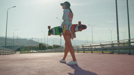 mujer caminando con longboard en el parque de la ciudad
