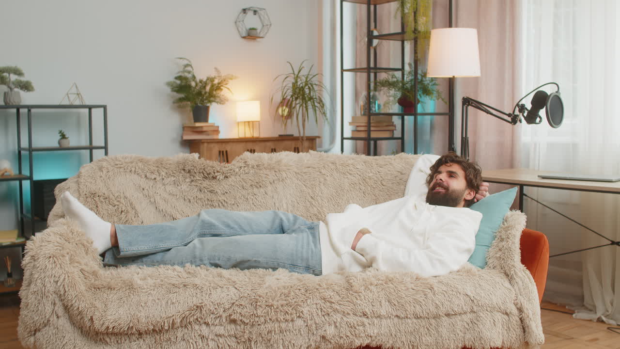 지친 인디언 잘생긴 젊은 남자는 집 아파트의 거실에서 소파에 누워 휴식을 즐기고 있습니다.