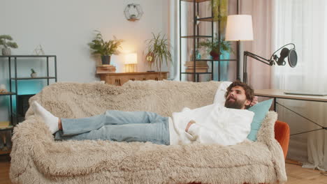 tired indian handsome young man guy enjoy relaxing lying on sofa in living room at home apartment