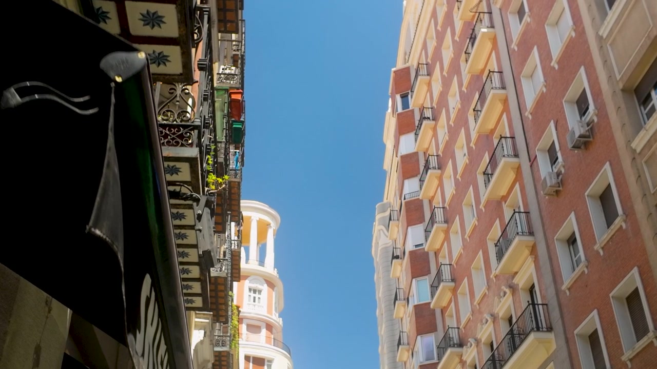 Perspectiva de baixo ângulo mostrando varandas espanholas históricas e edifícios de apartamentos modernos contra um céu azul claro em Madrid. Cena urbana autêntica para conteúdo de viagens e imóveis.