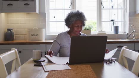una mujer afroamericana mayor estresada usando una computadora portátil y calculando las finanzas en casa