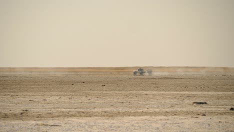 long tracking shot of an off-road vehicle crossing the dry and barren terrain of the makgadikgadi salt pan in botswana with the shimmer of a mirage glinting under the hot african sun