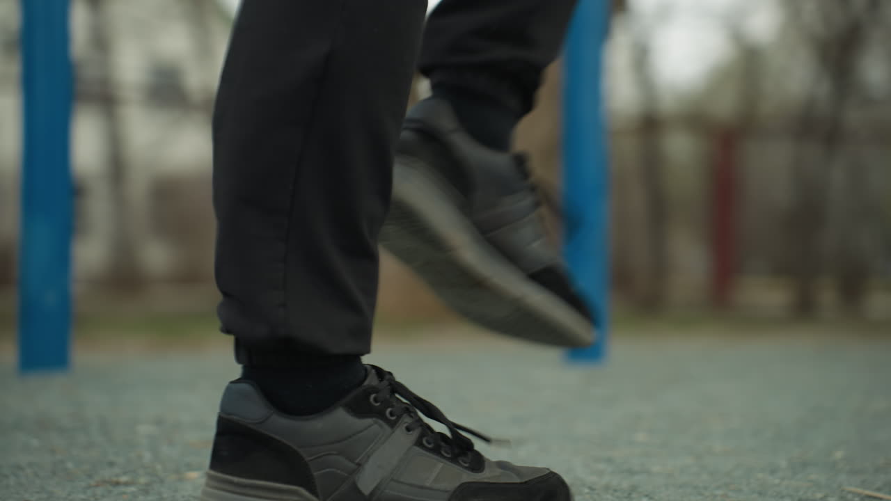 Close-up of a person s legs jogging quickly, wearing black jeans and black sneakers, with a blurred view of blue iron bars in the background