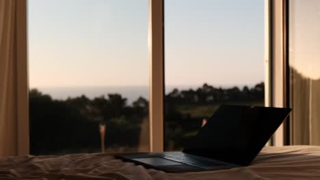 portátil en la cama con ventana abierta con vistas a la vegetación escénica y el océano