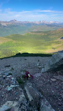 vertical view, female hiker climbing up on rocky hill above beautiful landscape on sunny summer day