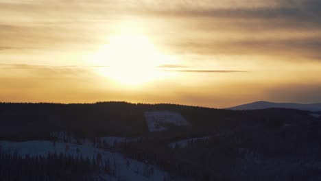 High-angle-shot-over-snow-covered-highlands-with-coniferous-trees-in-Beitostolen,-village-in-Oystre-Slidre-Municipality-in-Innlandet-county,-Valdres,-Beito,-Norway-with-sunset-in-background