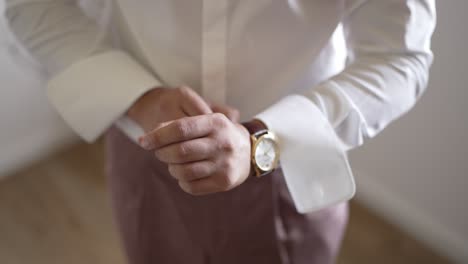 man adjusting cufflinks wearing white shirt and gold watch showcasing groom preparation on wedding morning