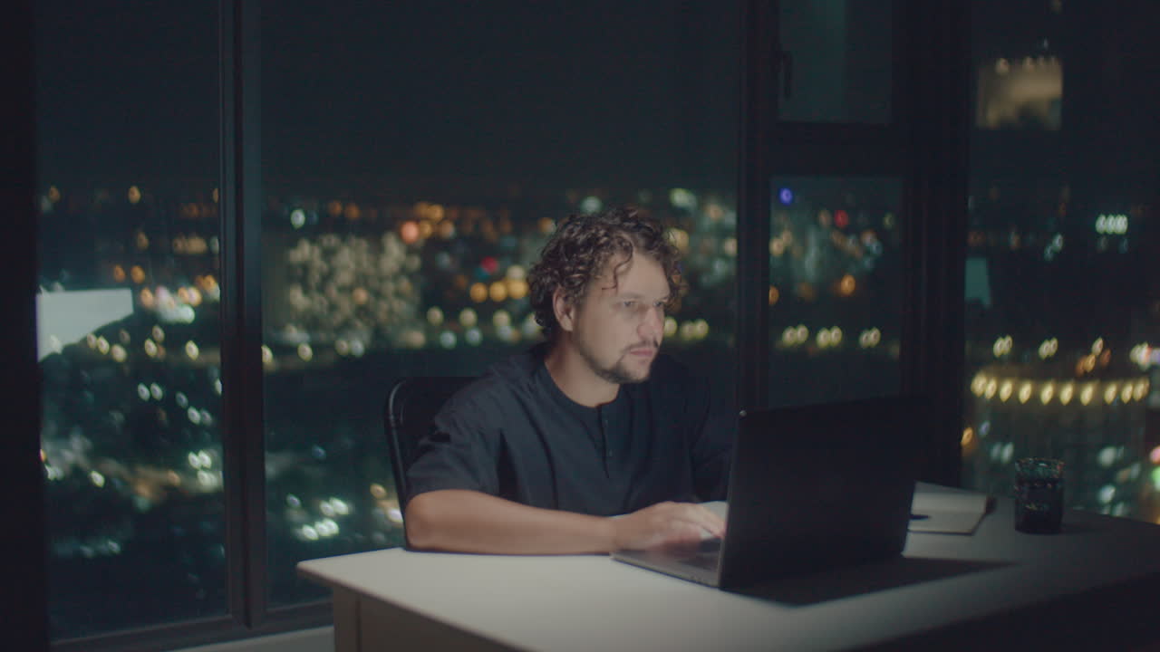 curly-haired man works at a computer at night