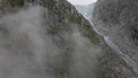 Rocky-Mountains-Mit-Wolken-An-Der-Seite-Und-Enthüllung-Eines-Majestätischen-Gletschers,-Drohnenaufnahme-Aus-Der-Luft