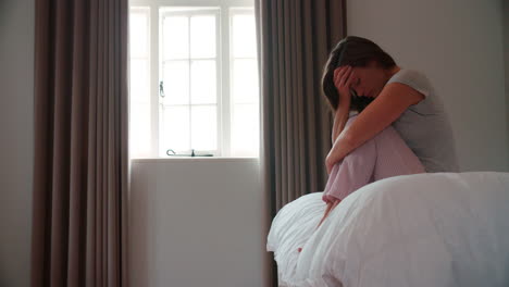 mujer que sufre de depresión sentada en la cama en pijama