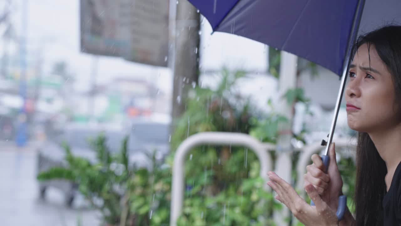 아름다운 젊은 아시아 여성이 에 들고 있는 우산에서 물방울을 모으기 위해 팔을 고, 불행하고 걱정하는 여성 노동자가 일에 늦어지고, 절망에 빠져, 거리의 보행자 길에 앉아, 비가 오는 계절.