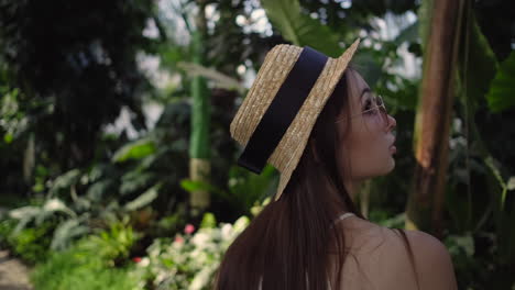 woman in a straw hat and sunglasses in a tropical greenhouse