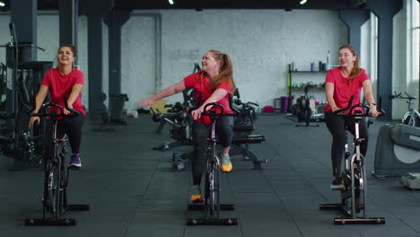 Group-of-smiling-friends-women-class-exercising,-training,-spinning-on-stationary-bike-at-modern-gym