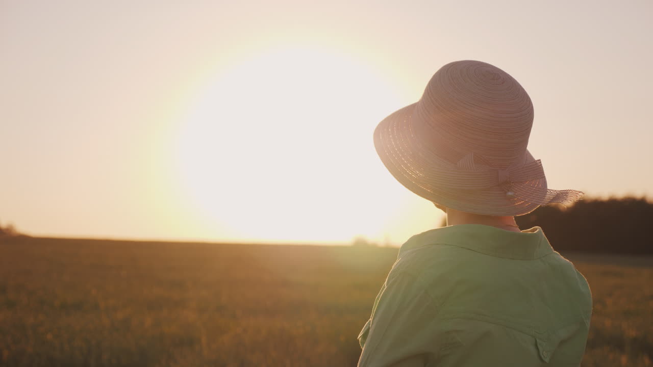 una agricultora con sombrero mira el horizonte sobre un campo de trigo disfrutando de la puesta de sol en la parte posterior vi