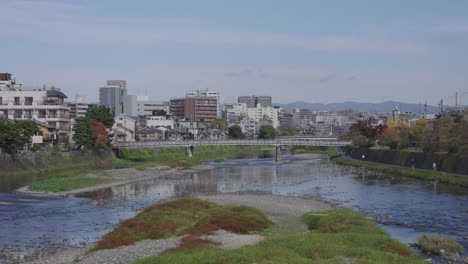 kamo river on warm clear day, kyoto city in background, japan