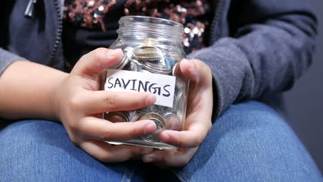 child girl holding a coin jar while sited