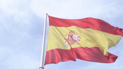 Plano-Detallado-De-La-Bandera-Española-Ondeando-En-El-Viento-En-Cámara-Lenta-Con-Cielo-Azul-Y-Nubes-En-El-Fondo-Primer-Plano-De-La-Bandera-Española