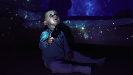 baby gazing at starry night projection in dark room