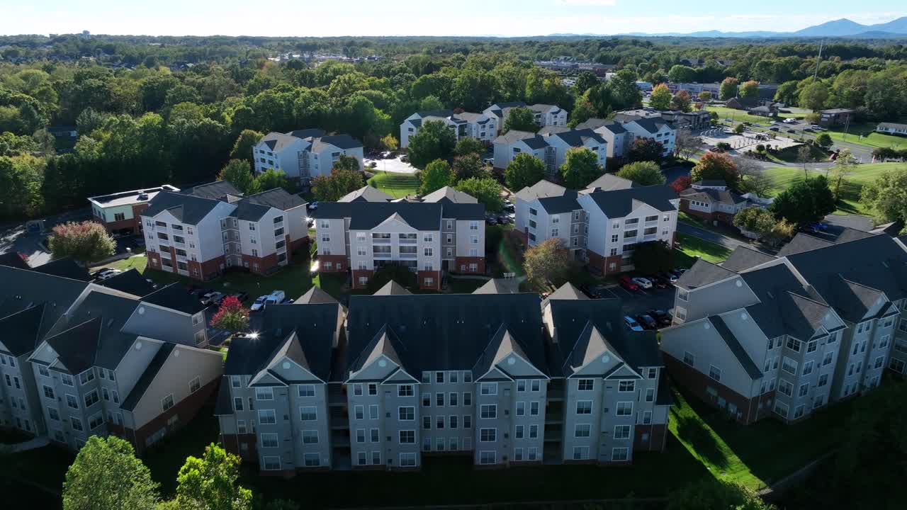 Aerial establishing shot of american suburb neighborhood with townhouses, multi-family units and apartment buildings at sunset. Peaceful evening in fall season. Green trees in USA