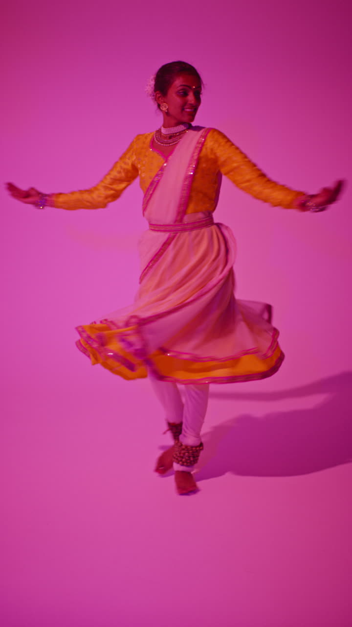 video vertical de larga duración en estudio de una bailarina de kathak que realiza un baile vestida con el vestido tradicional indio contra un fondo púrpura 6